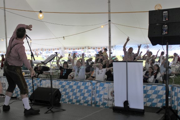 A man onstage leads the crowd in the dance for Bobfahrer Lied (the bobsled song)